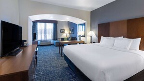 Une chambre d’hôtel dotée d’un grand lit, d’un bureau avec un téléviseur à écran plat, d’un coin salon avec un canapé et des fauteuils, et d’un mur incurvé avec une fenêtre.