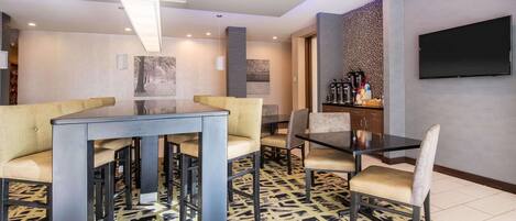 A modern dining area with a glass-top table, cushioned chairs, and a patterned rug.