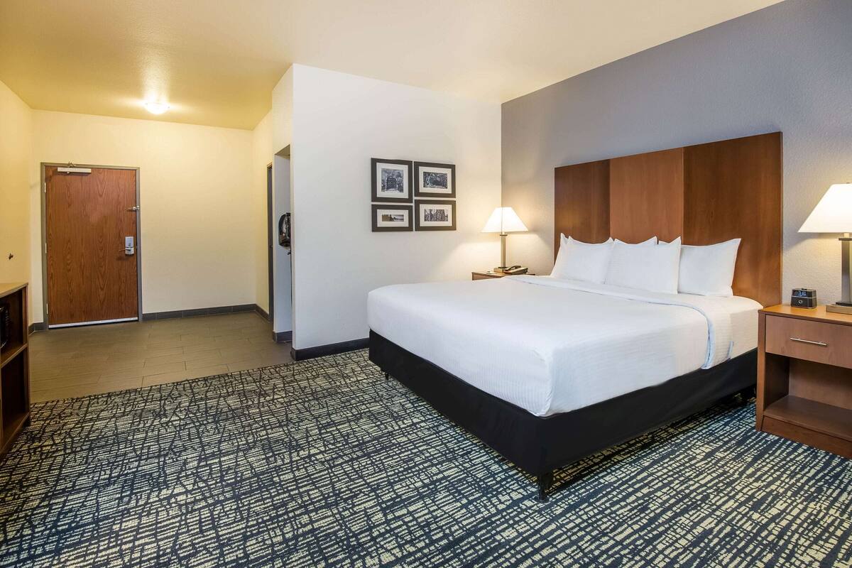 A hotel room with a large bed, a wooden headboard, a bedside table with a lamp, and a wall-mounted TV.