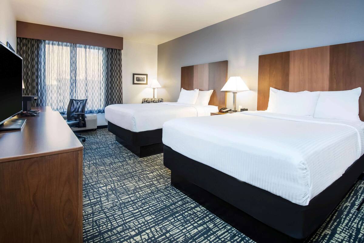 A hotel room with two beds, a desk, a TV, and a window with curtains.