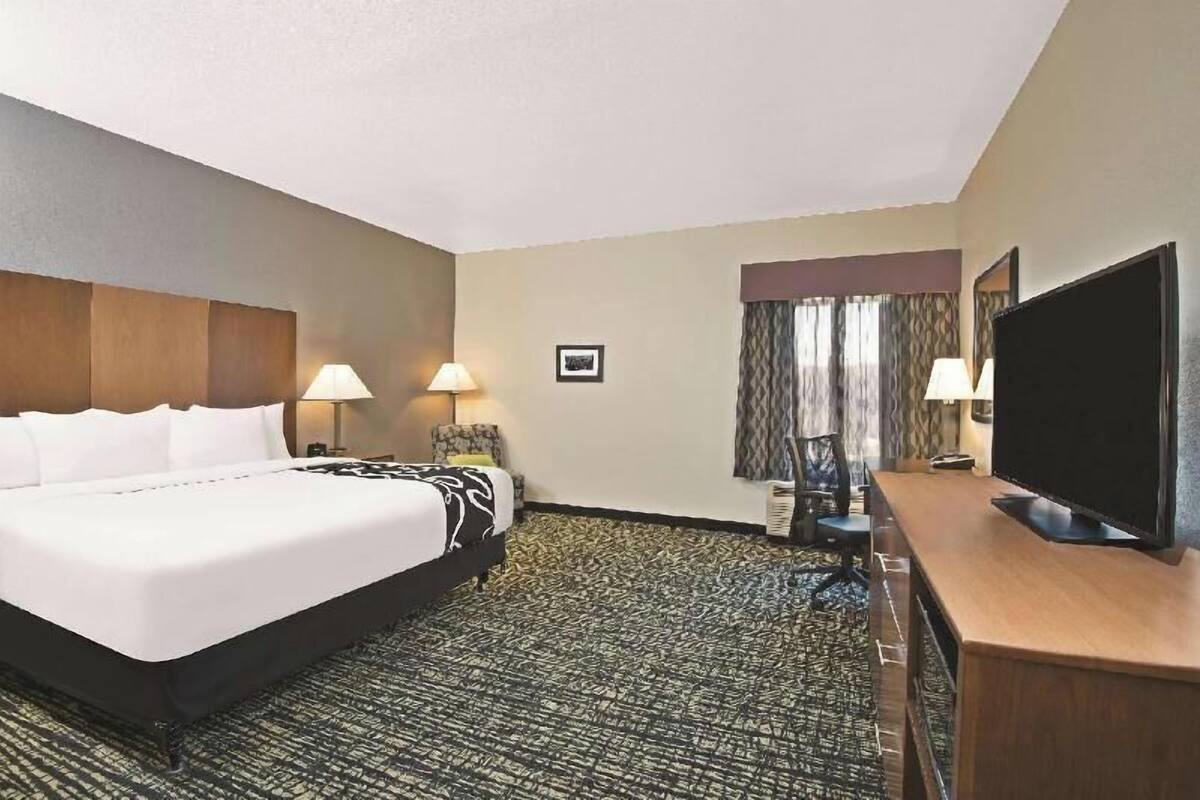 A hotel room with a large bed, two bedside lamps, a flat-screen TV, a desk, and a patterned carpet.
