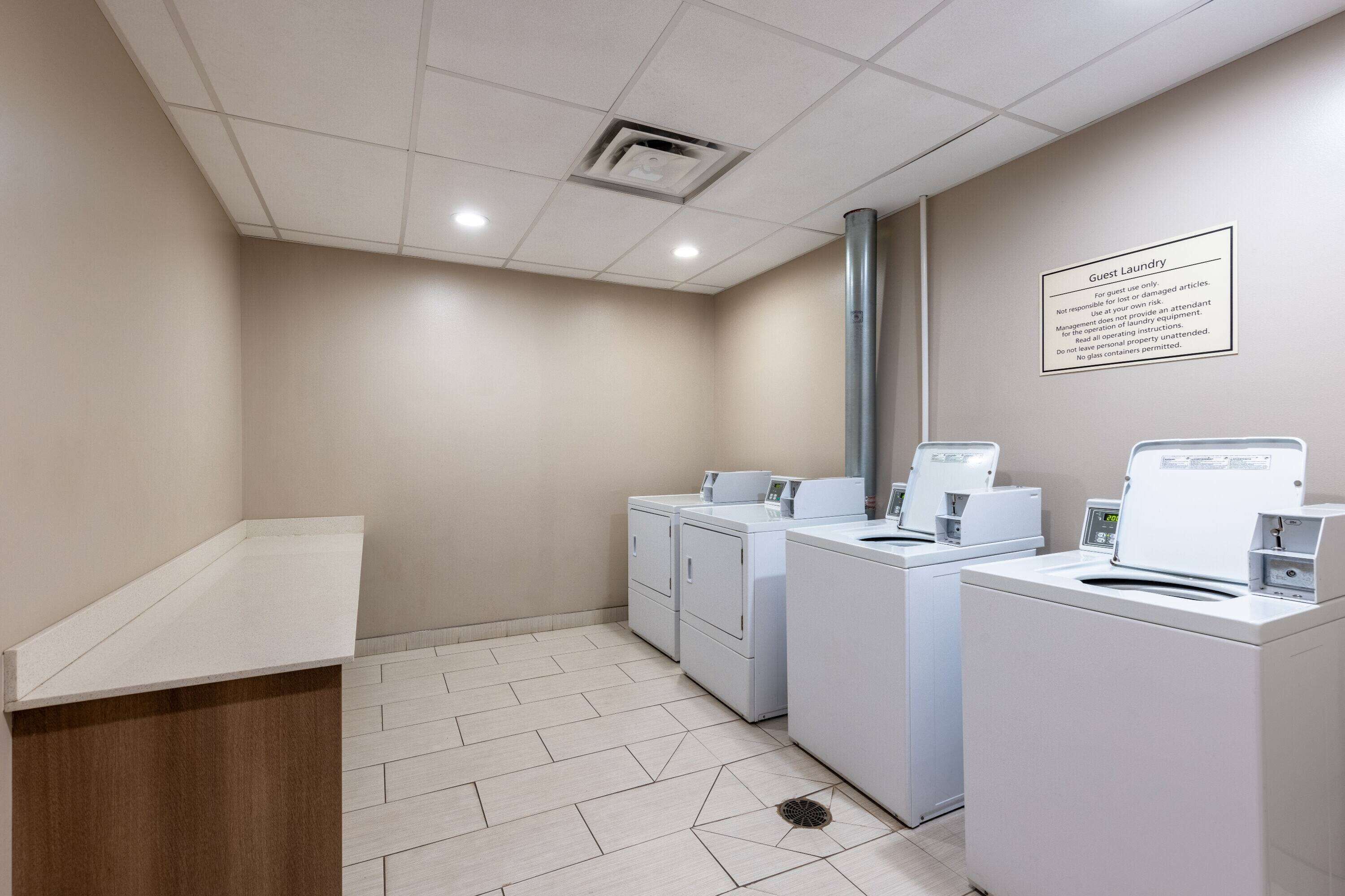 A guest laundry area with a sign detailing usage rules, a sink, and three washing machines.