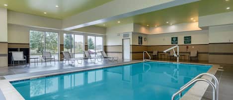 Una gran piscina interior con paredes de vidrio transparente, sillones de descanso y un cartel de prohibición de saltos.