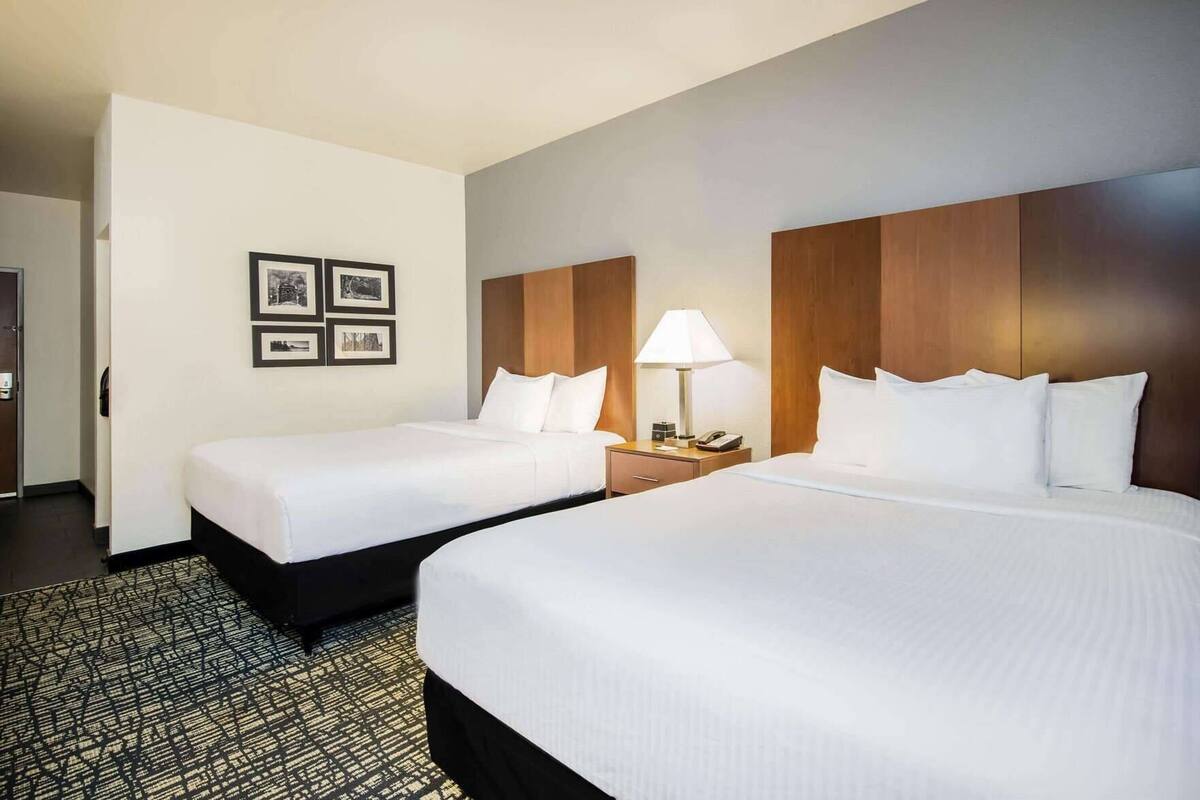 A hotel room with two beds, a nightstand with a lamp, and a wall with framed pictures.