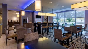 Un espace repas moderne, doté de tables et de chaises, d’un bar et de grandes fenêtres offrant une vue sur l’extérieur.