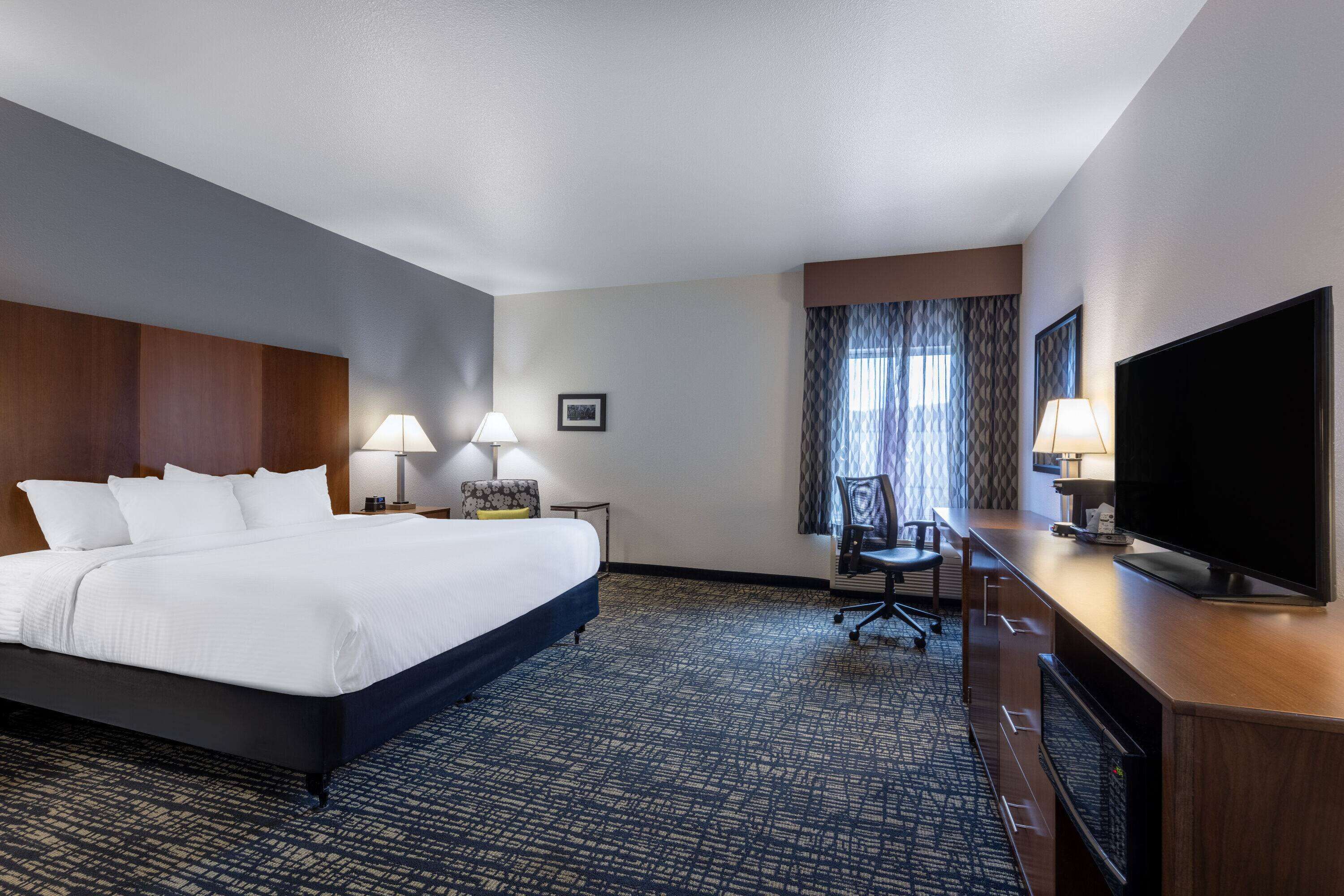 Une chambre d’hôtel avec un grand lit, un bureau avec une télévision et une fenêtre avec des rideaux.