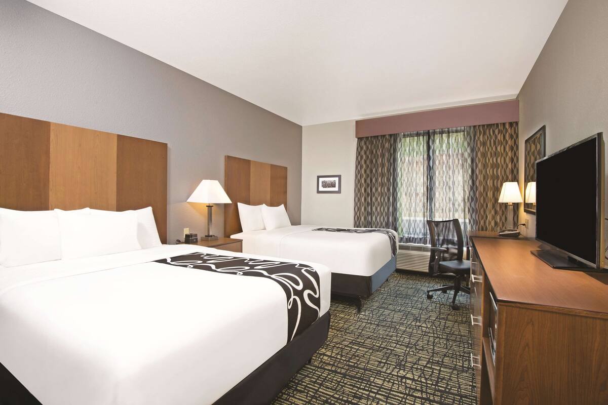 A hotel room with two beds, a desk with a TV, and a chair.