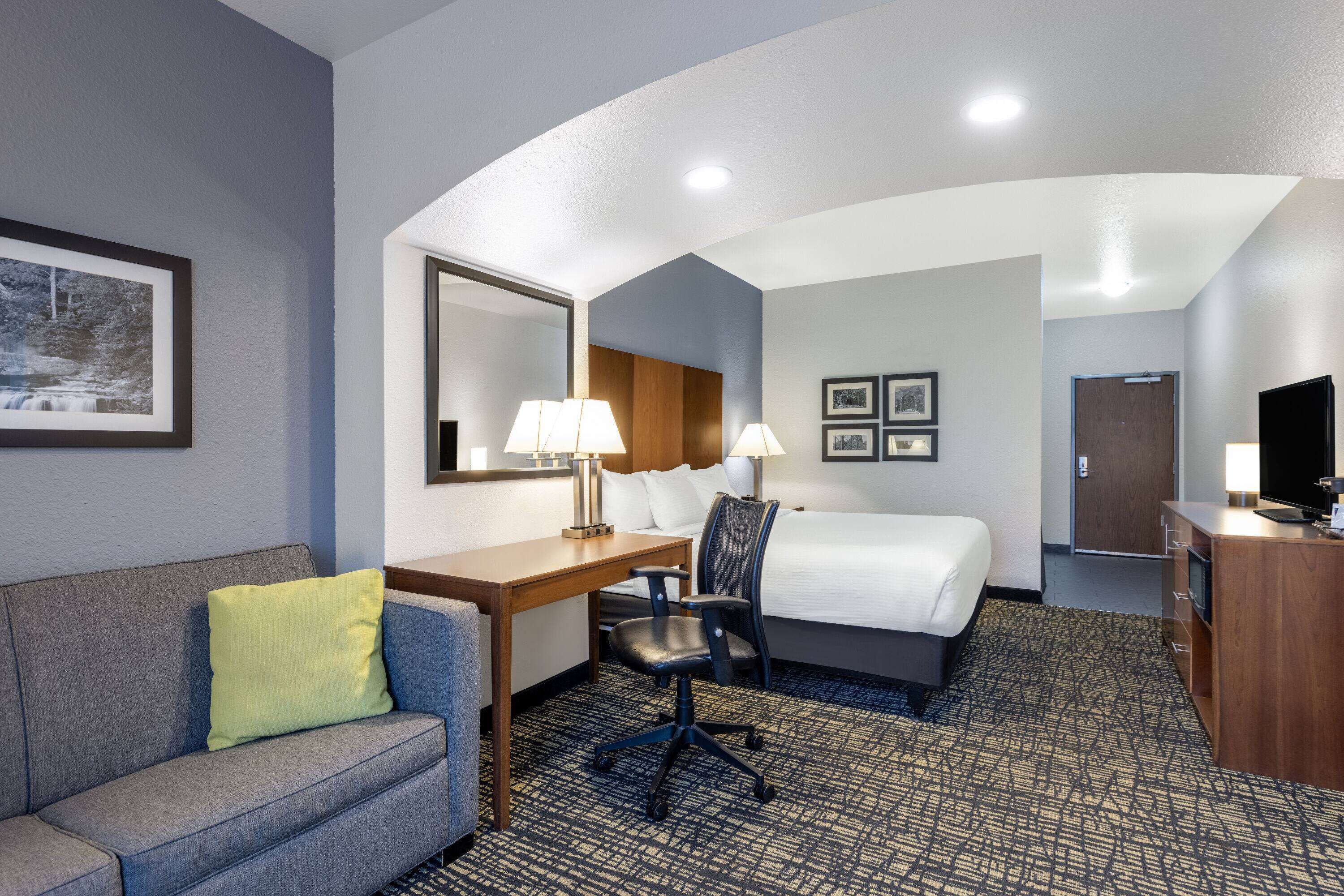 A hotel room with a bed, desk, chair, and a television.