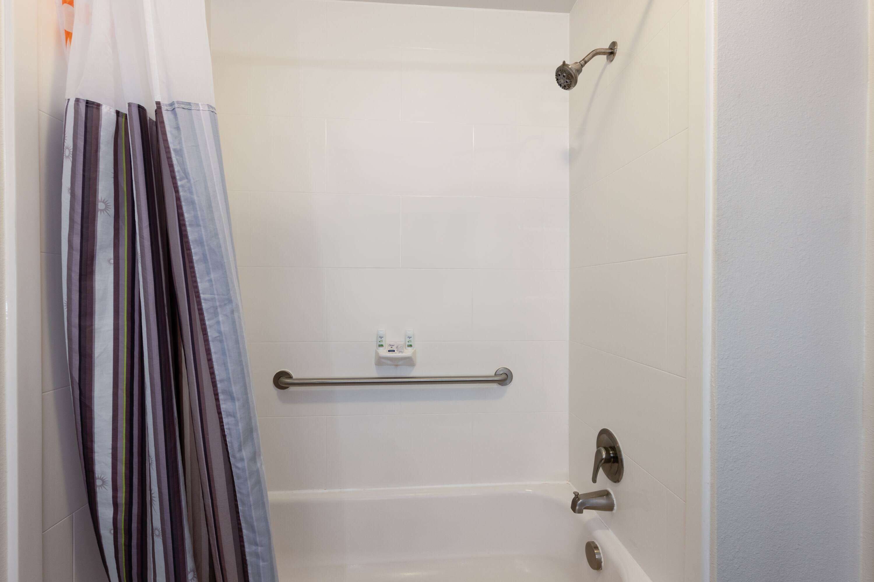 A shower area with a grab bar, a white bathtub, and a shower curtain.