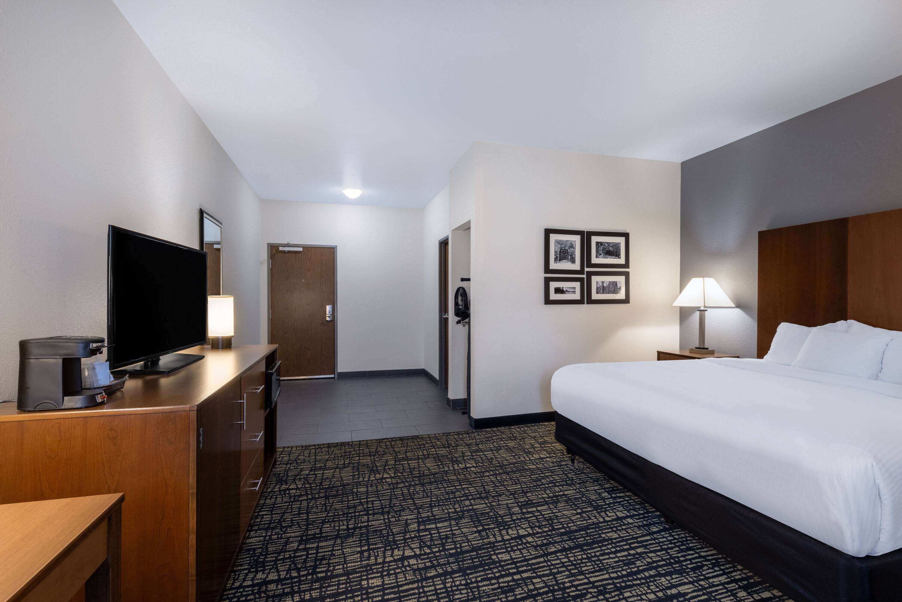 Ein Hotelzimmer mit Bett, Fernseher, Schreibtisch mit Lampe und einer Tür zu einem weiteren Raum.
