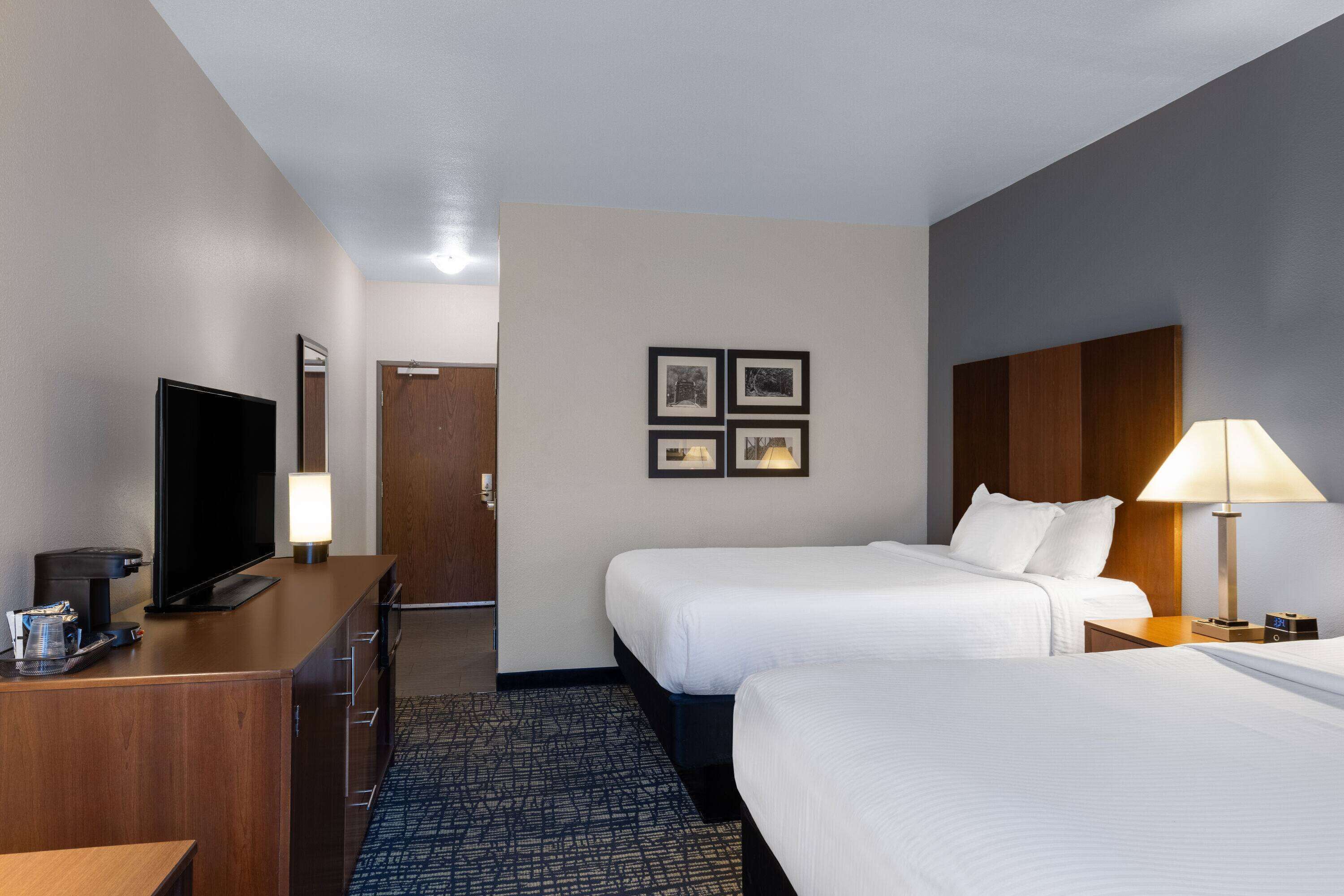 Habitación de hotel con dos camas, un escritorio con televisor, cafetera y lámpara.
