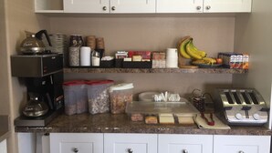 A kitchen with white cabinets, a coffee machine, a toaster, and various food items on the counter.