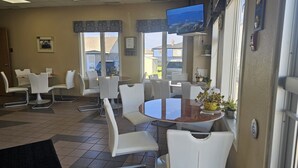 A restaurant with white chairs and tables, a TV mounted on the wall, and a view of the outside.