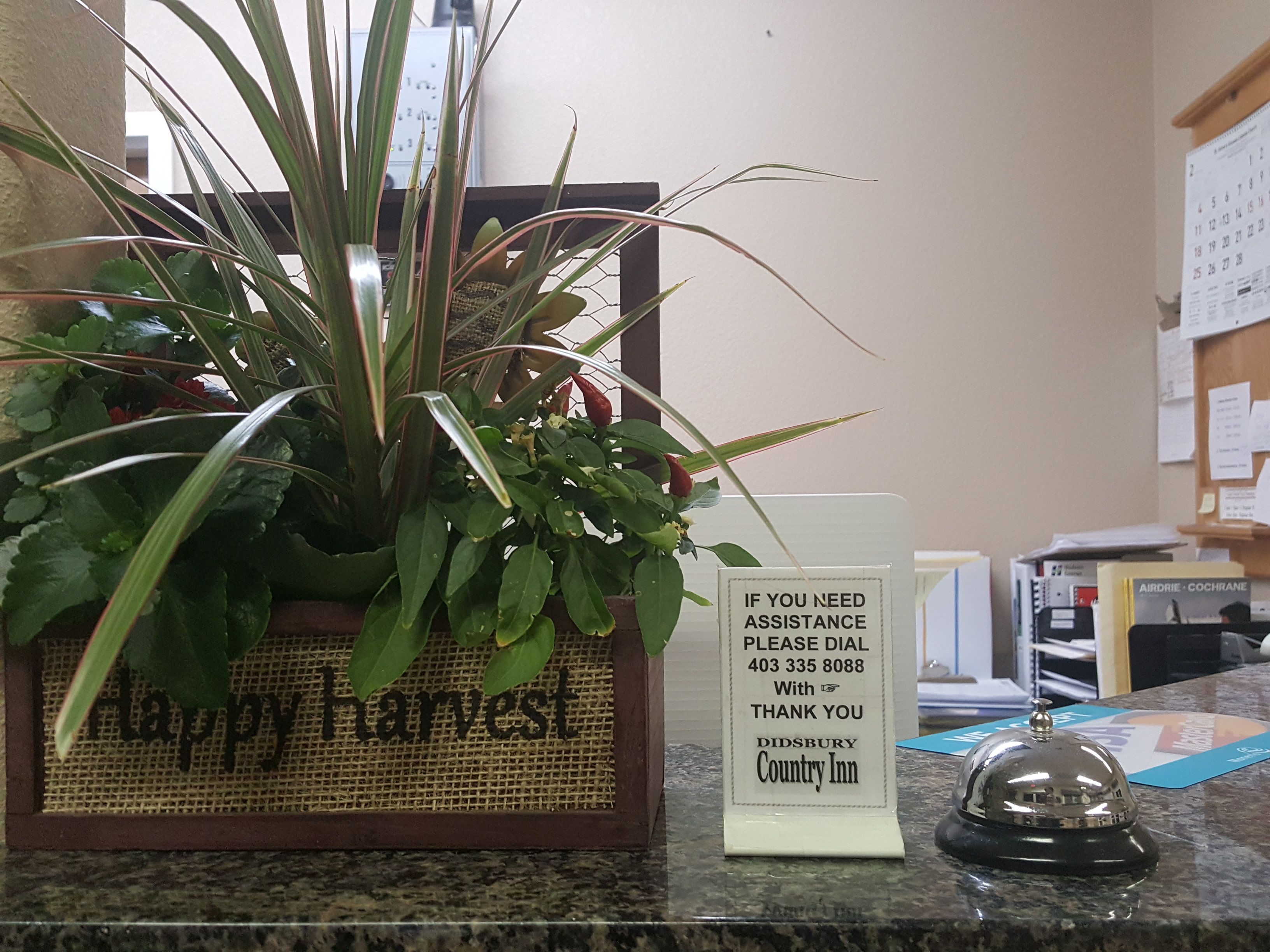 Una recepción con un cartel que dice 'Happy Harvest', una planta en maceta, un cartel que indica 'Si necesita asistencia' y una campana.