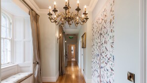 A hallway with a wooden floor, a bench, a chandelier, and a wall with bird illustrations.
