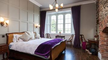 A traditional bedroom with a large bed, a wooden floor, a brick wall, and a window with curtains.