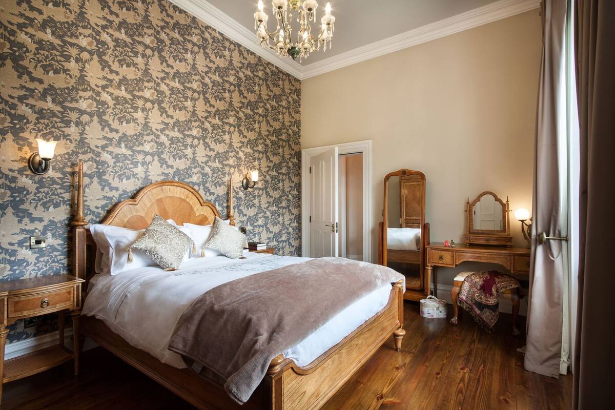 Un dormitorio con cama de madera, una mesita de noche, un aparador, un espejo y una araña.