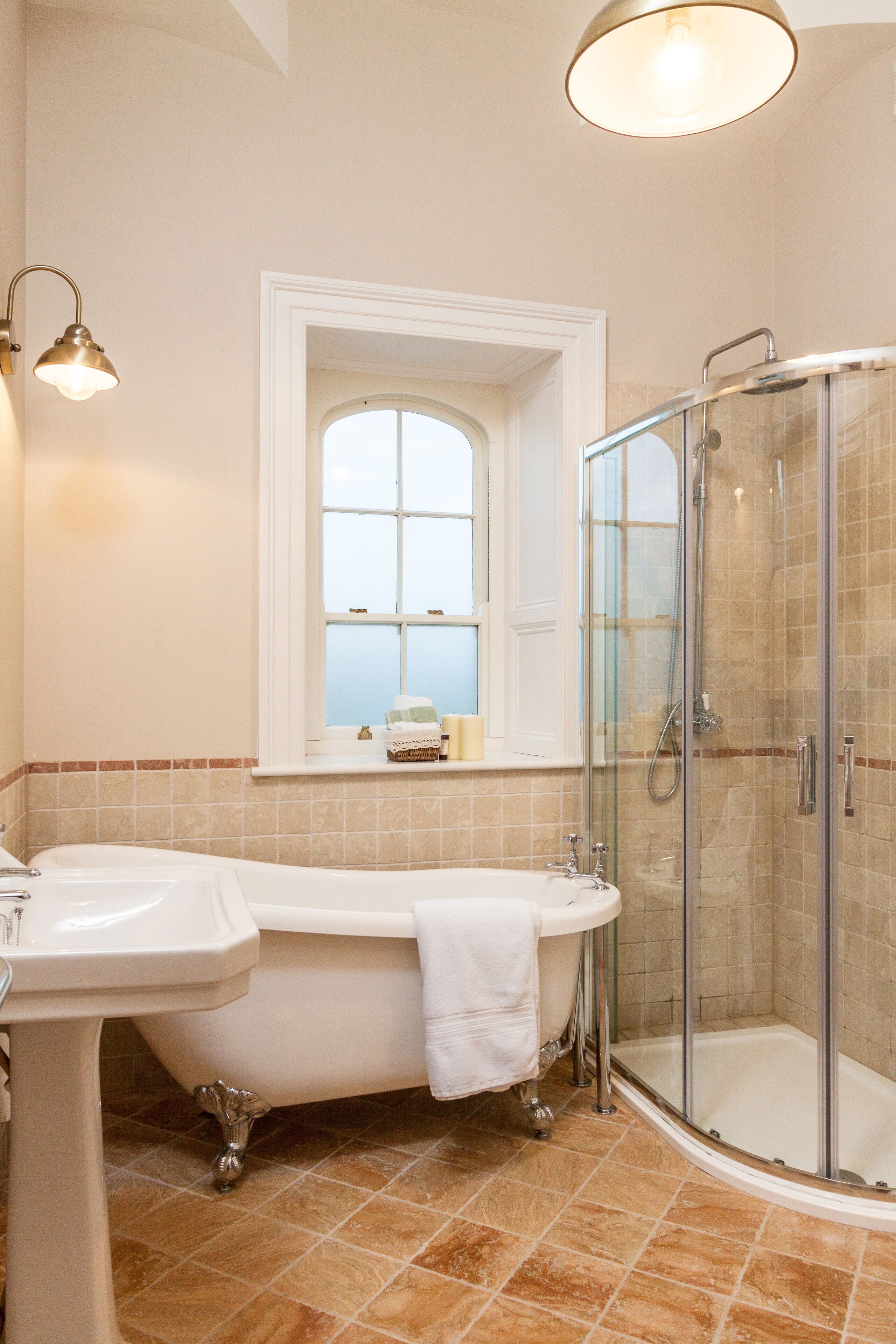 A bathroom with a bathtub, a sink, a glass-enclosed shower, and a window with a view.