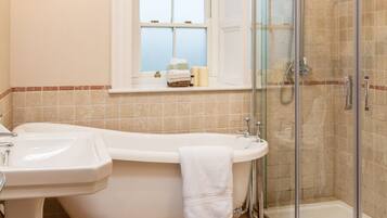 A bathroom with a bathtub, a sink, a glass-enclosed shower, and a window with a view.
