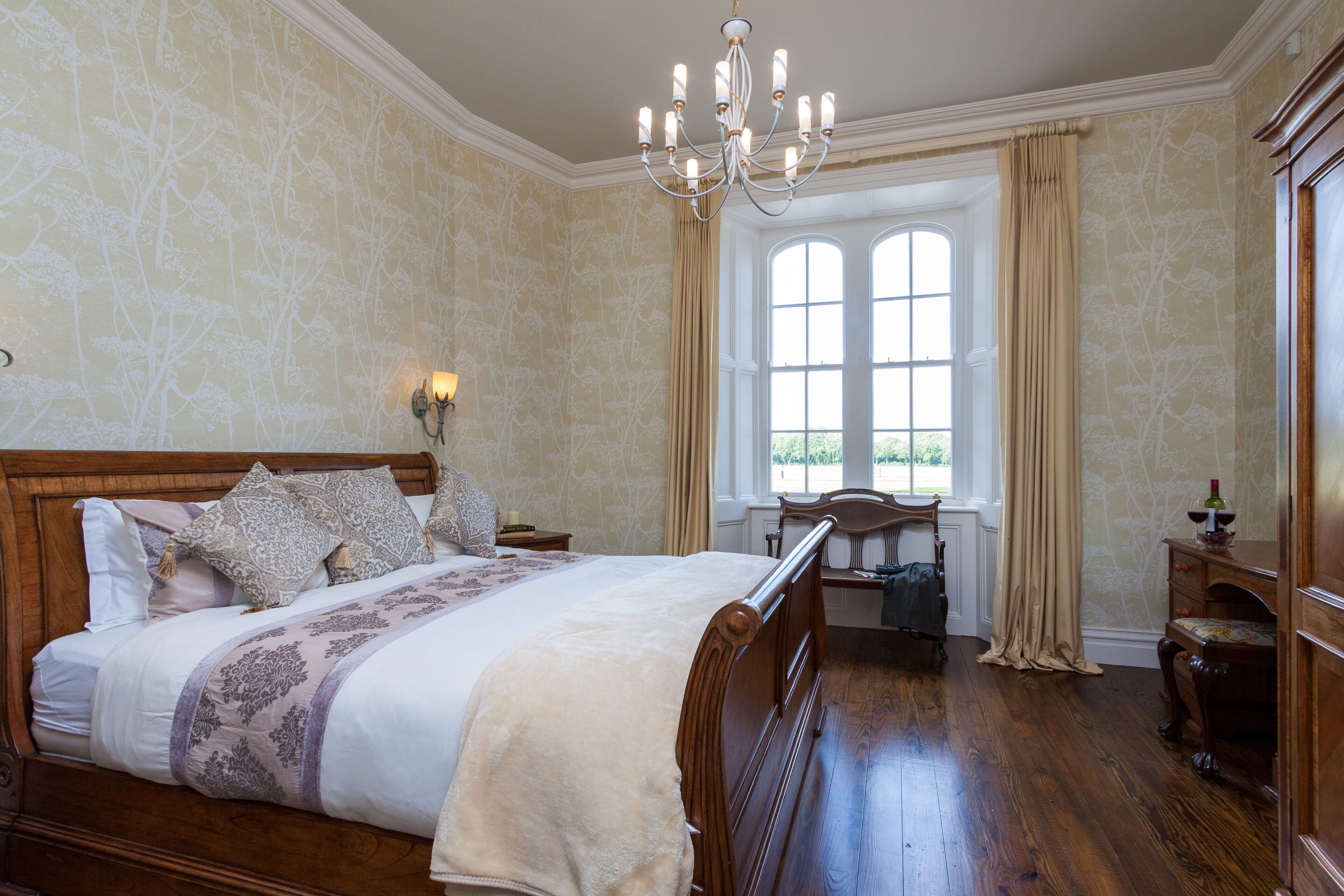 A bedroom with a large bed, a chandelier, a window with curtains, and a wooden dresser.