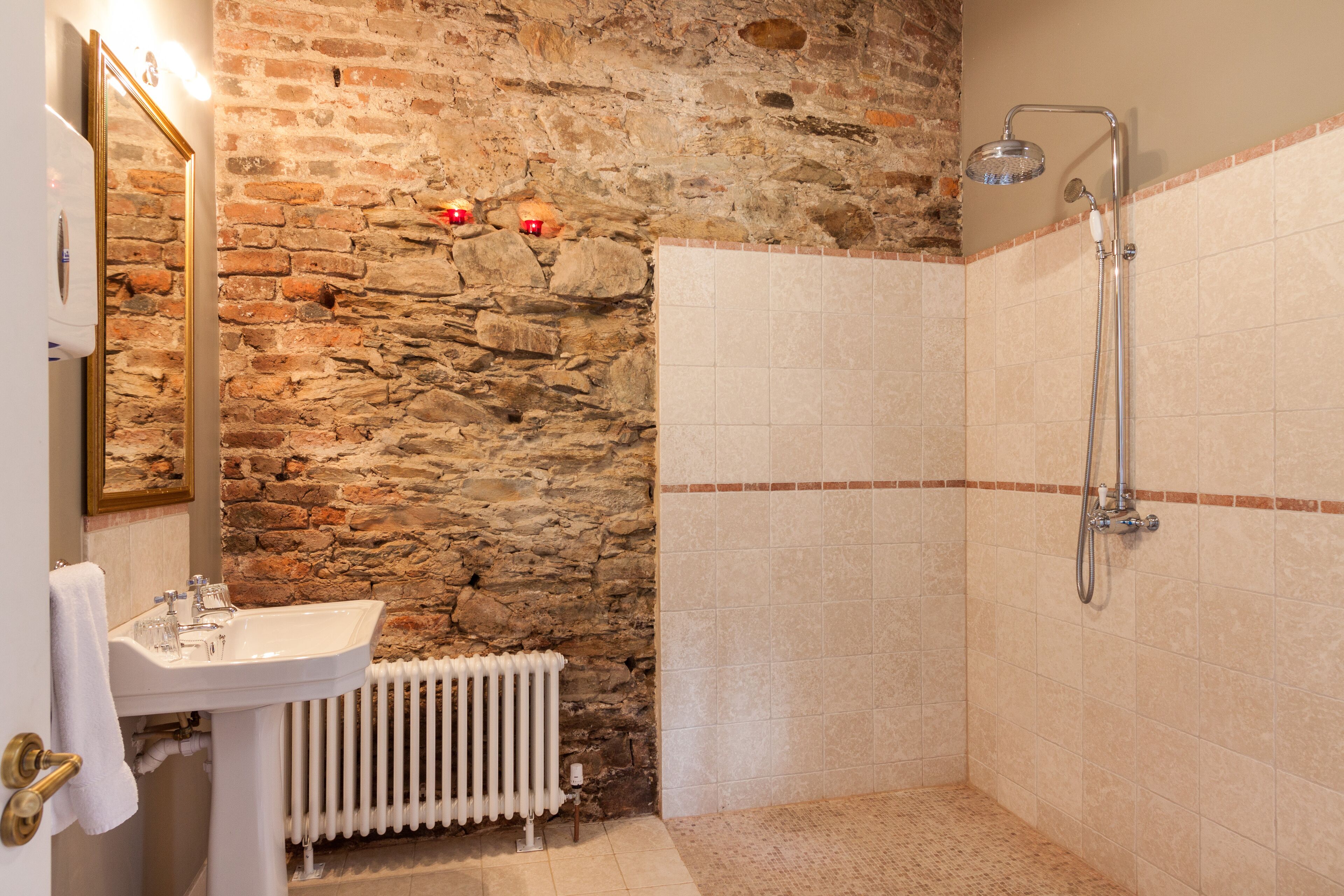 A bathroom with a stone wall, a white sink, and a shower.