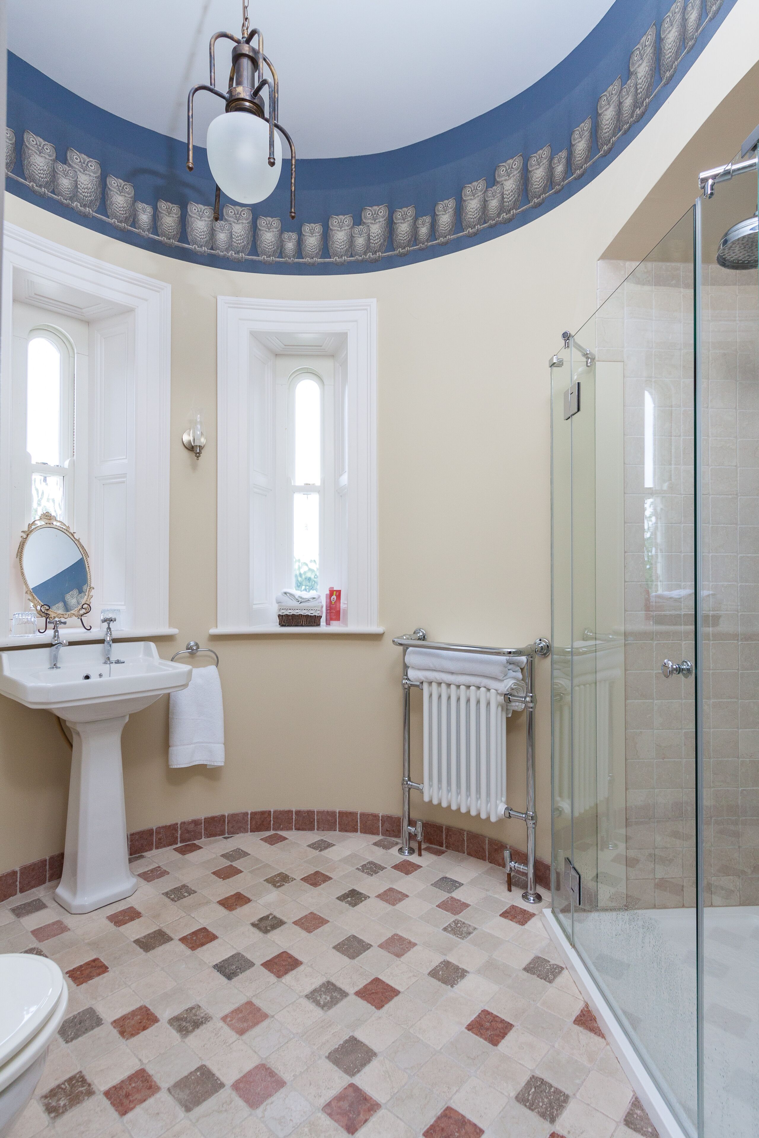 A bathroom with a white sink, mirror, and toilet, a glass shower enclosure, and a patterned floor.