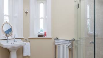 A bathroom with a white sink, mirror, and toilet, a glass shower enclosure, and a patterned floor.
