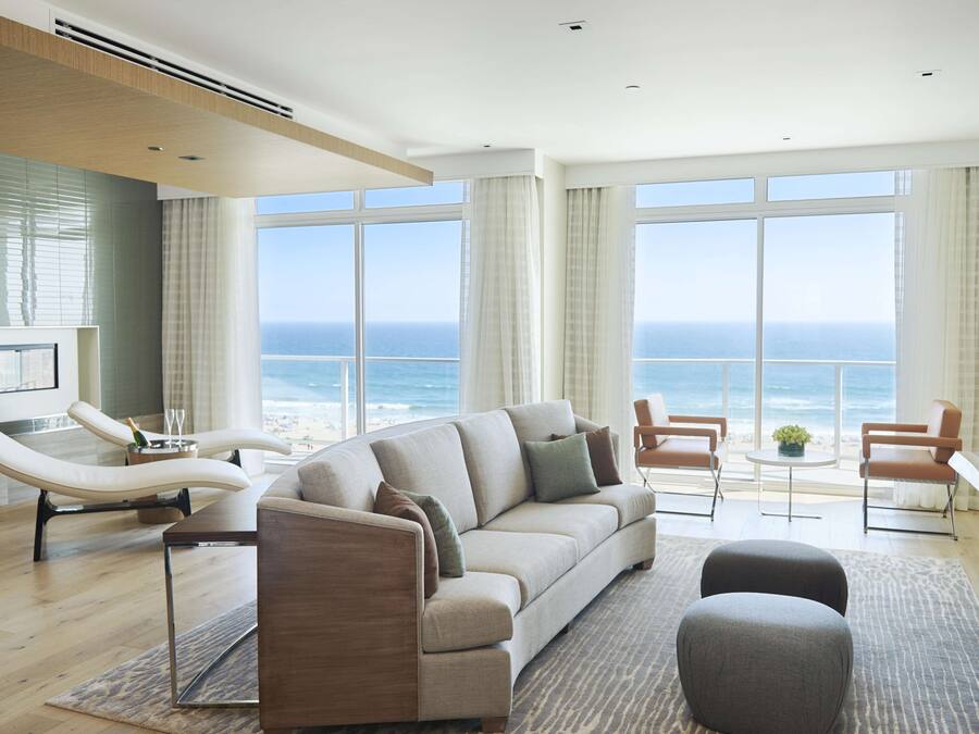 A modern living room with a large window overlooking the ocean, a curved sofa, two armchairs, and a small table with a plant.