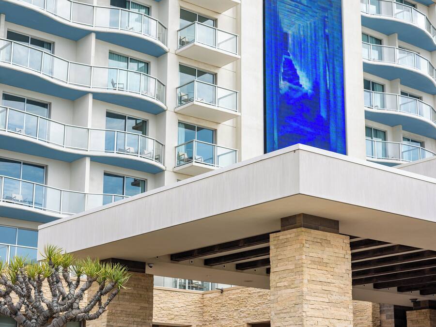 A blue van with "PASÉA HOTEL & SPA" signage parked in front of a hotel with multiple balconies and a large digital display.