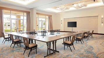 A conference room with a long table, chairs, a flat-screen TV, and large windows with curtains.