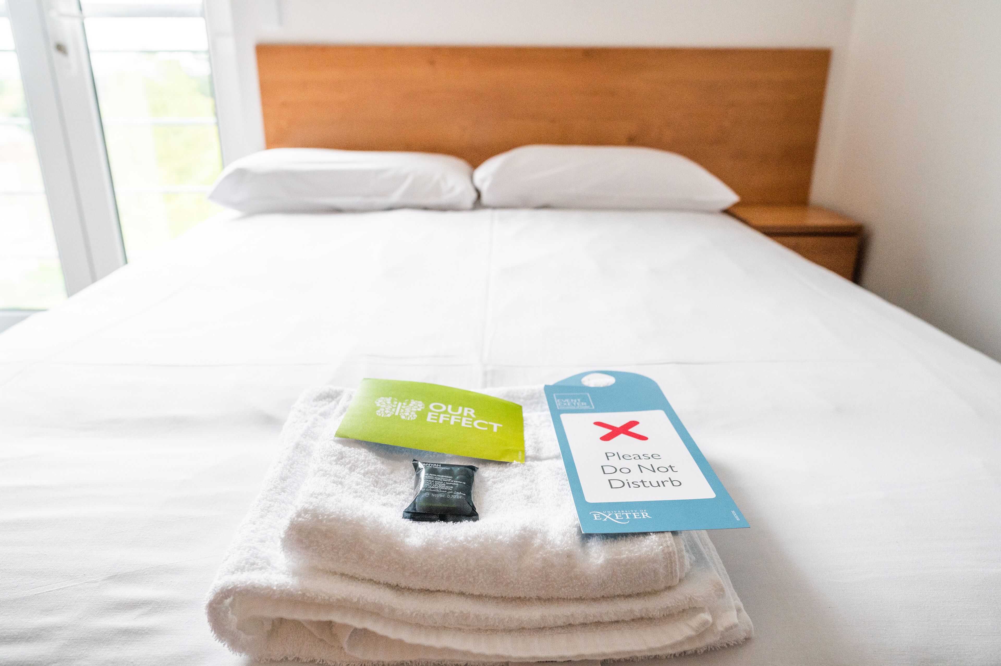 A neatly made bed with a folded towel and a tag that reads "Please Do Not Disturb."