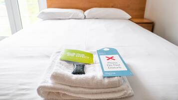 A neatly made bed with a folded towel and a tag that reads "Please Do Not Disturb."