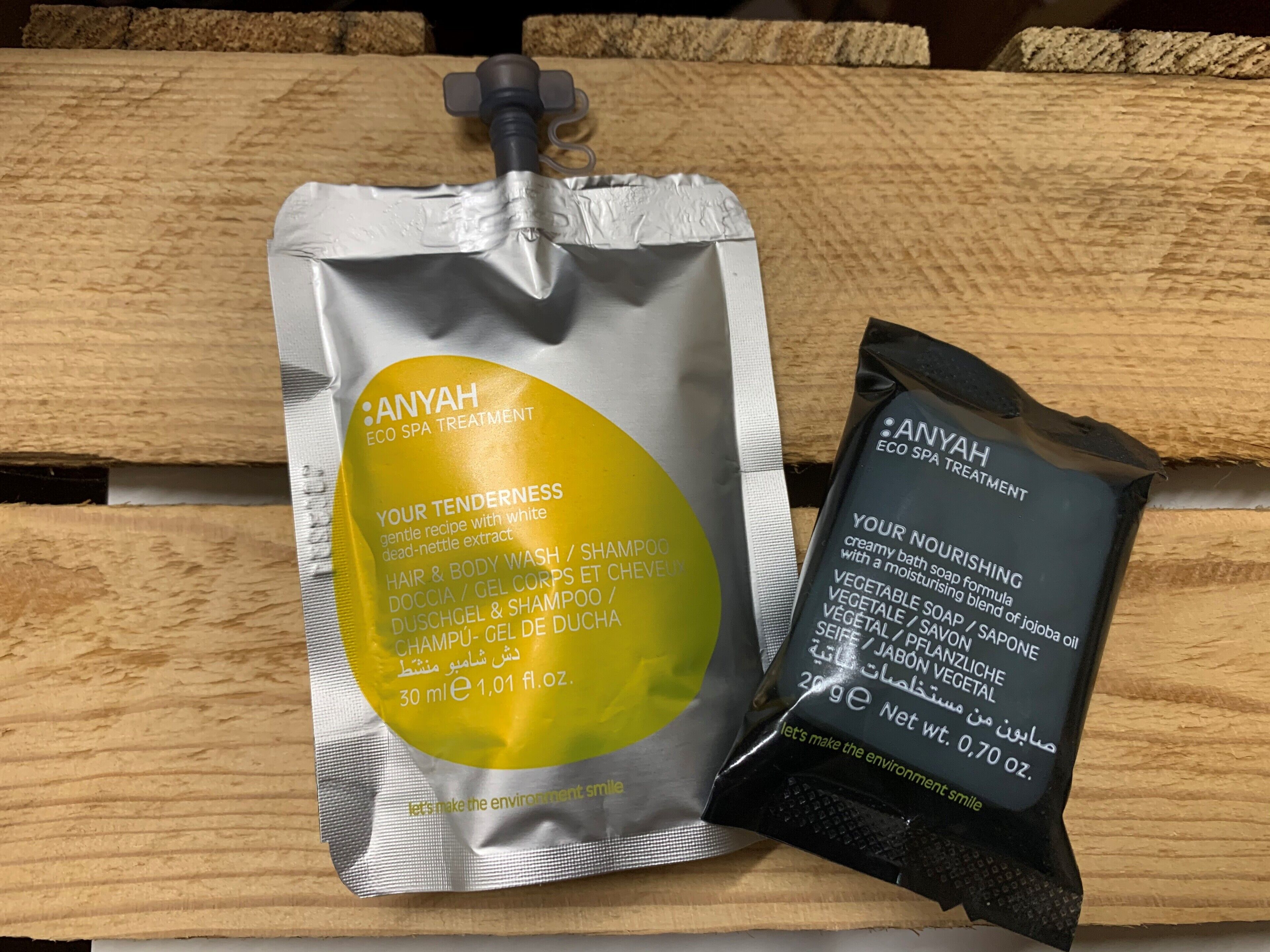 Zwei Anyah Eco Spa Treatment Produkte, eine Haarkörperwäsche/Shampoo sowie eine nährende Körperseife, auf einer Holzoberfläche.
