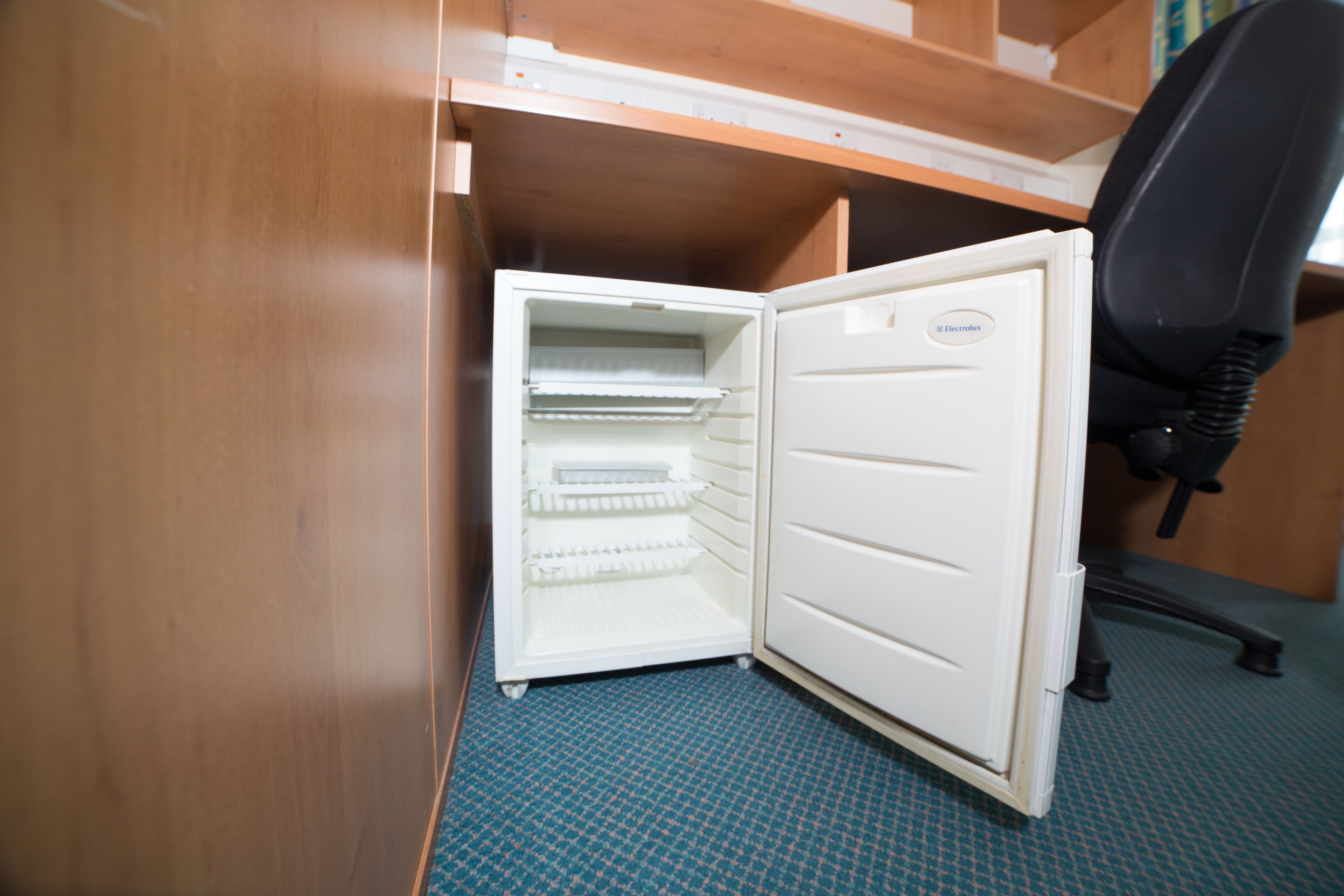 Un refrigerador compacto con varias repisas, situado en una habitación que tiene un escritorio de madera y una silla de oficina negra.