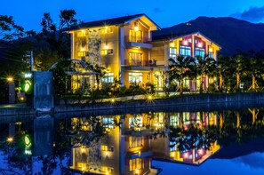 Un hotel de varios pisos con balcones, piscina y montañas al fondo.