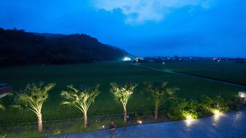 A nighttime view of a well-lit pathway with palm trees and a distant cityscape.