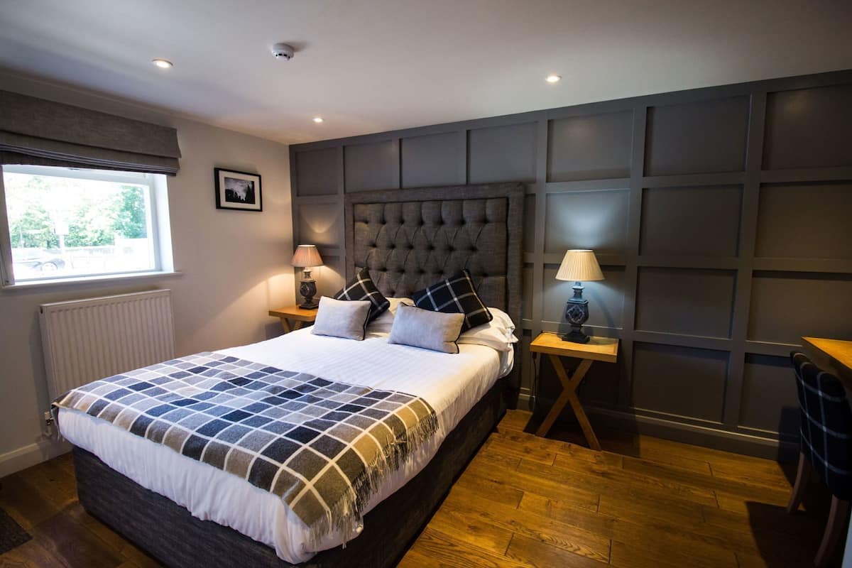 A bedroom with a large bed, two bedside tables with lamps, a window, and a radiator.