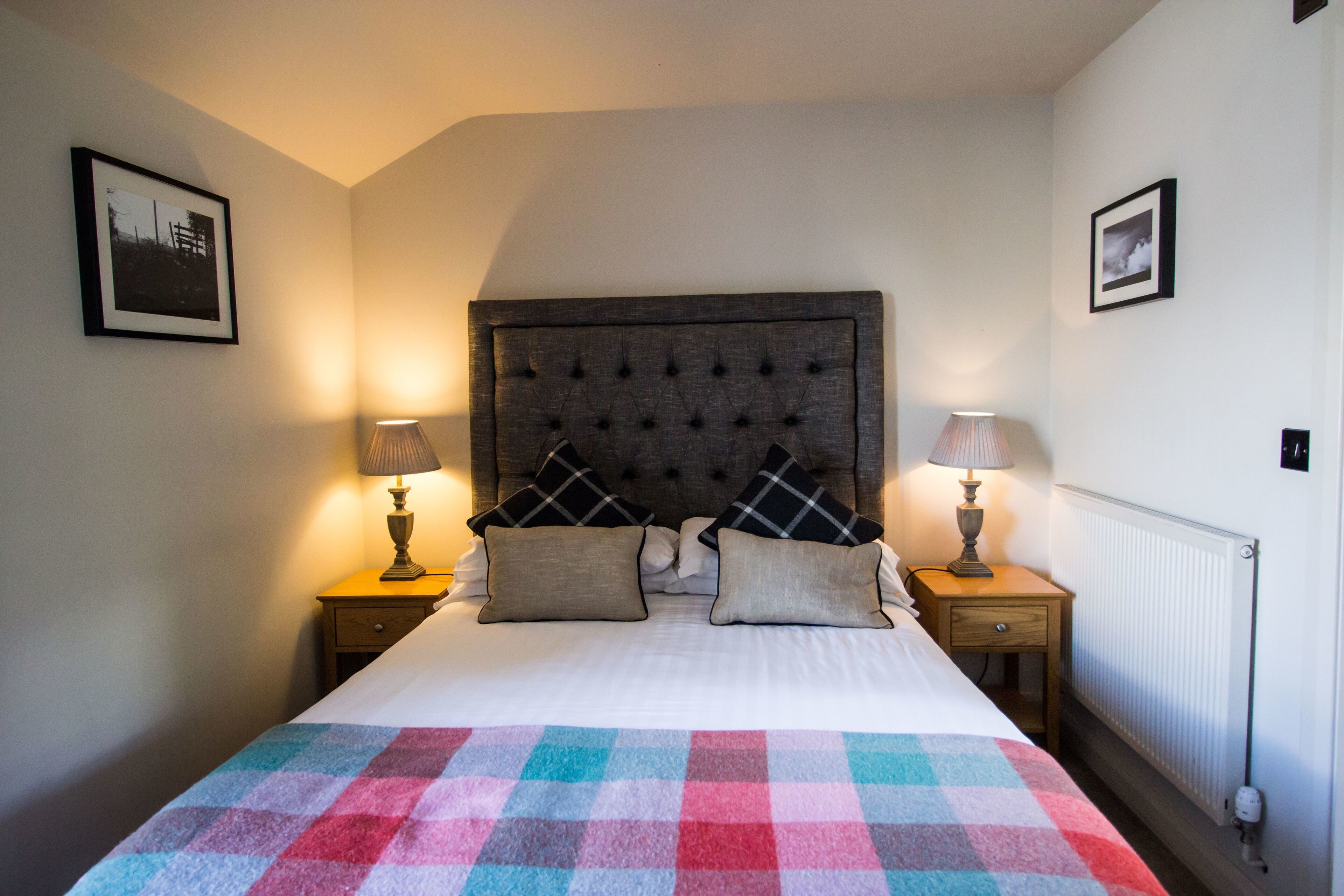 A neatly made bed with a colorful checkered blanket, two bedside lamps, and a headboard with a tufted design.