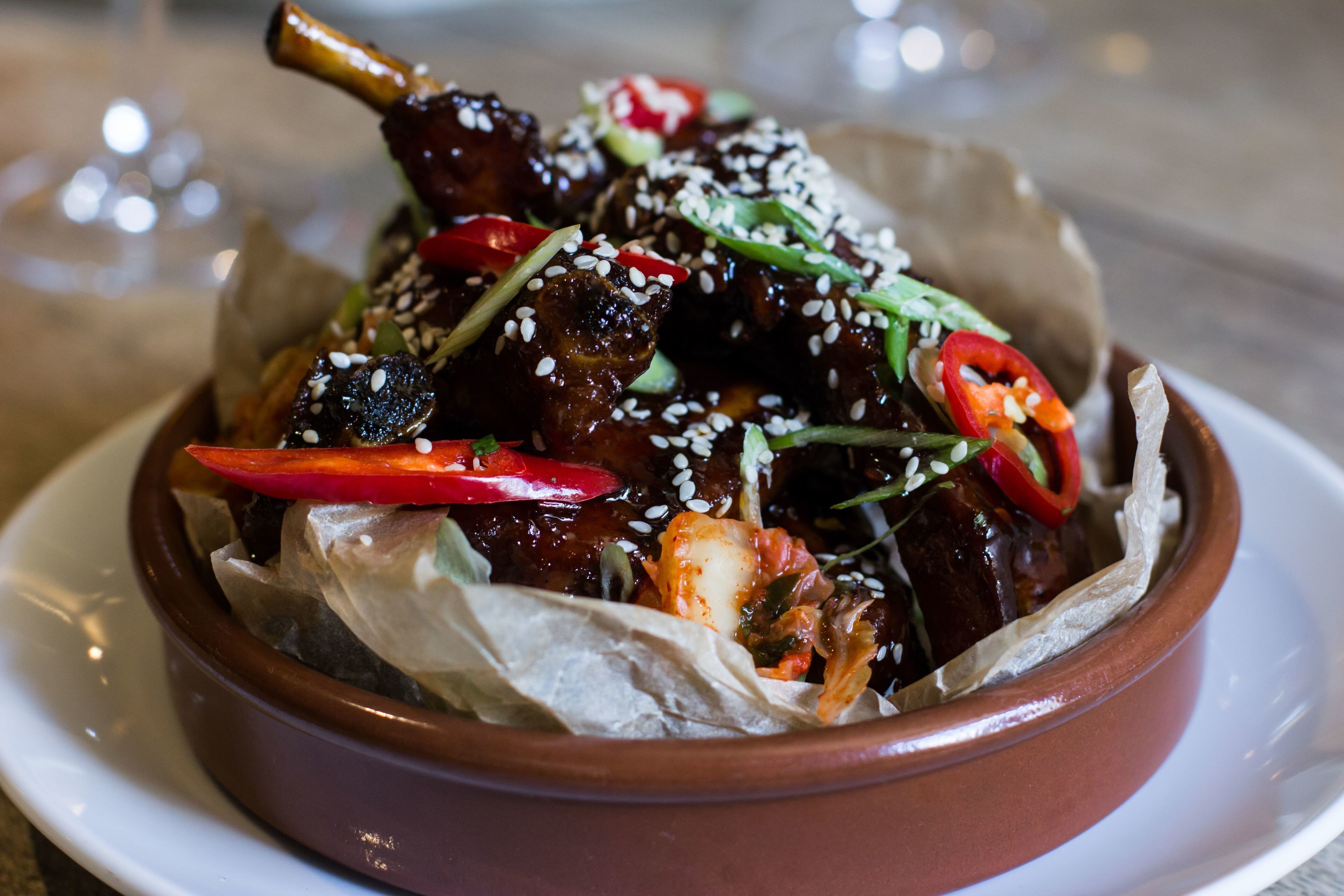 A dish of glazed meat with sesame seeds and sliced red peppers in a ceramic bowl.
