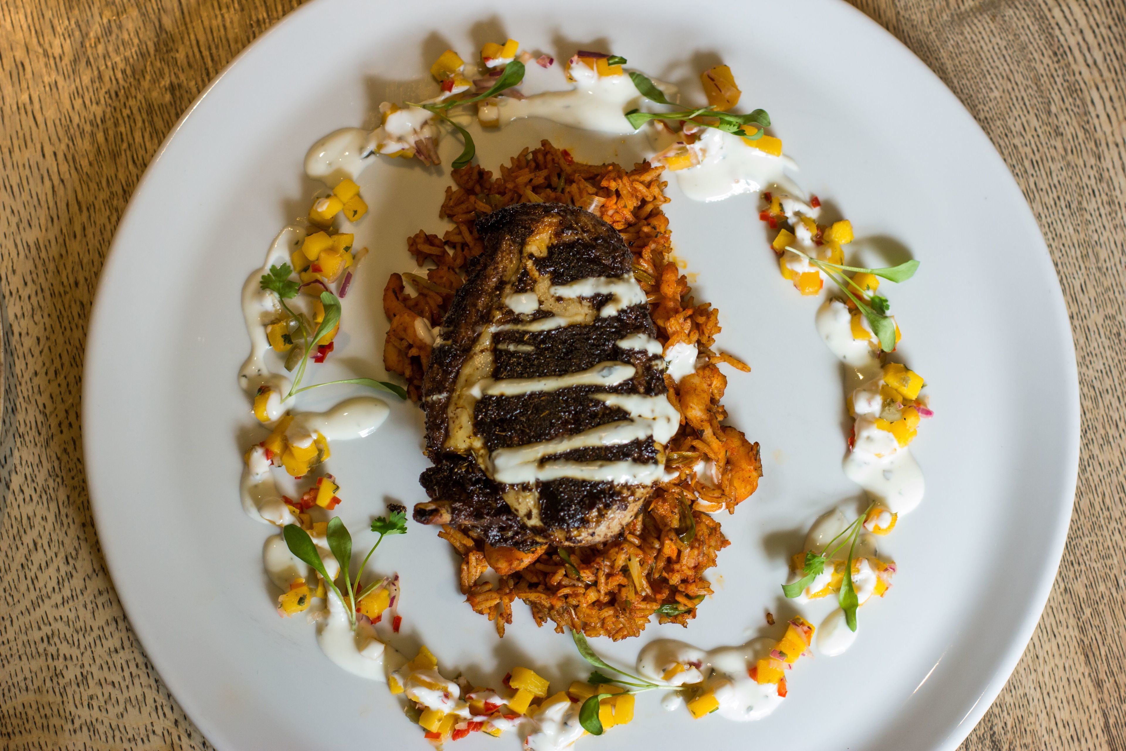 A plate of food with rice, a grilled meat, and a creamy sauce, garnished with herbs and diced vegetables.