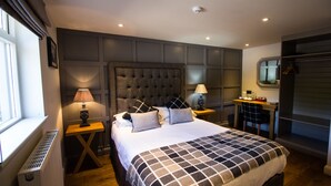 A modern bedroom with a large bed, two bedside tables with lamps, a dresser, and a window with blinds.