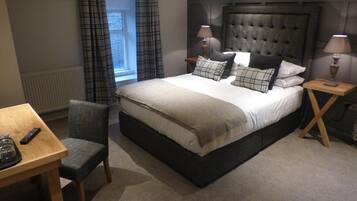 A bedroom with a large bed, two bedside tables, a chair, a small table, and a window with curtains.