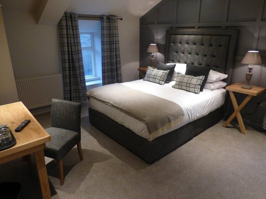 A bedroom with a large bed, two bedside tables, a chair, a small table, and a window with curtains.
