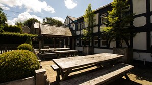 An outdoor seating area with wooden benches and picnic tables, surrounded by a traditional half-timbered building.
