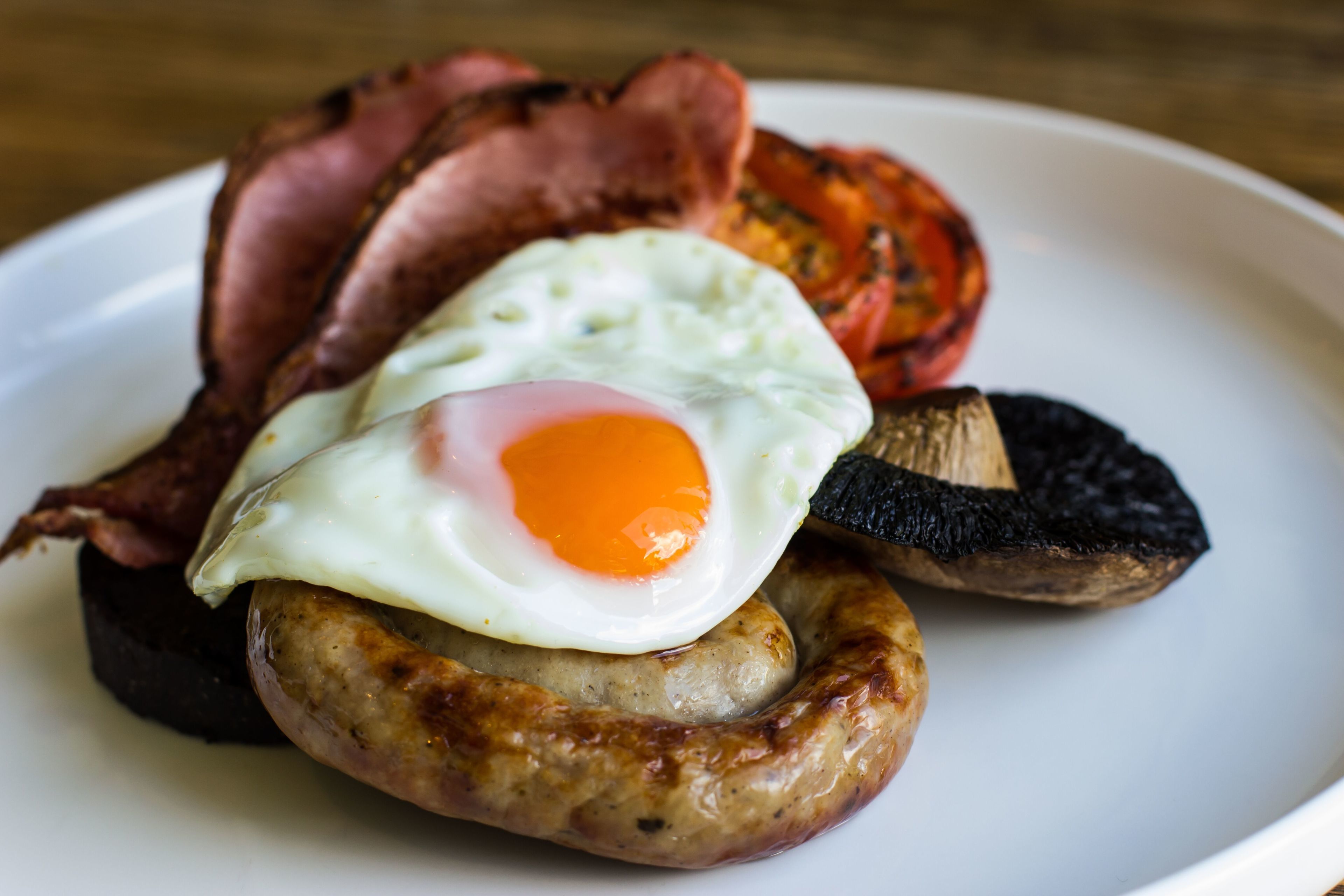 Une assiette avec une saucisse, un œuf au plat et une tranche de bacon.