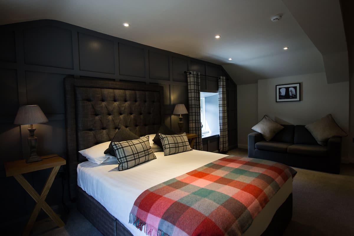 A bedroom with a large bed, a nightstand, a chair, and a window with curtains.