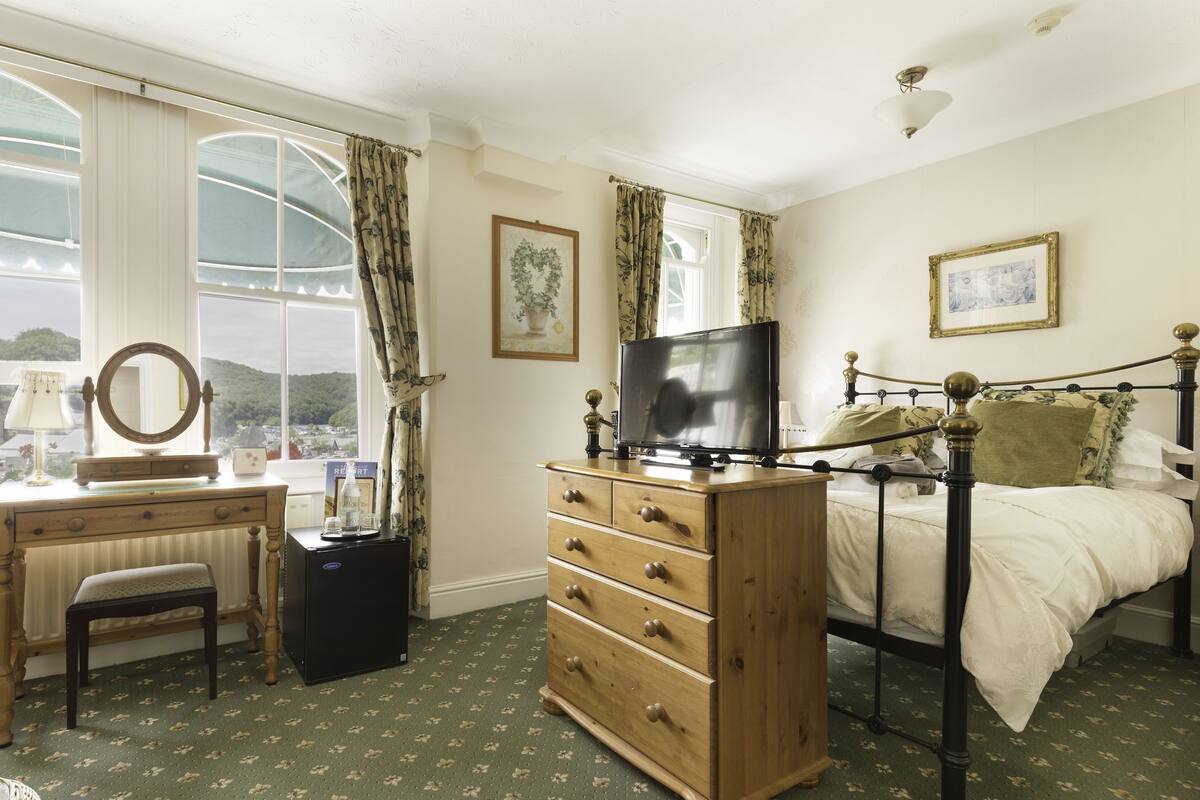 A bedroom with a bed, dresser, television, and a desk with a mirror.