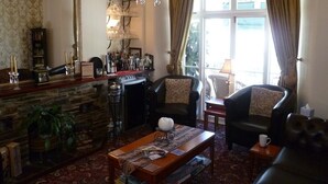 A cozy living room with a stone fireplace, leather armchairs, a coffee table with magazines, and a large mirror. - Dolphin Guest House (Looe)