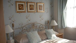 A bedroom with a bed, two bedside tables, a lamp, a nightstand, and a window with curtains. - Dolphin Guest House (Looe)