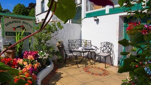 A patio area with a table and chairs, surrounded by potted plants and flowers. A sign reading "Dolphin House Reception" is visible in the background. - Dolphin Guest House (Looe)